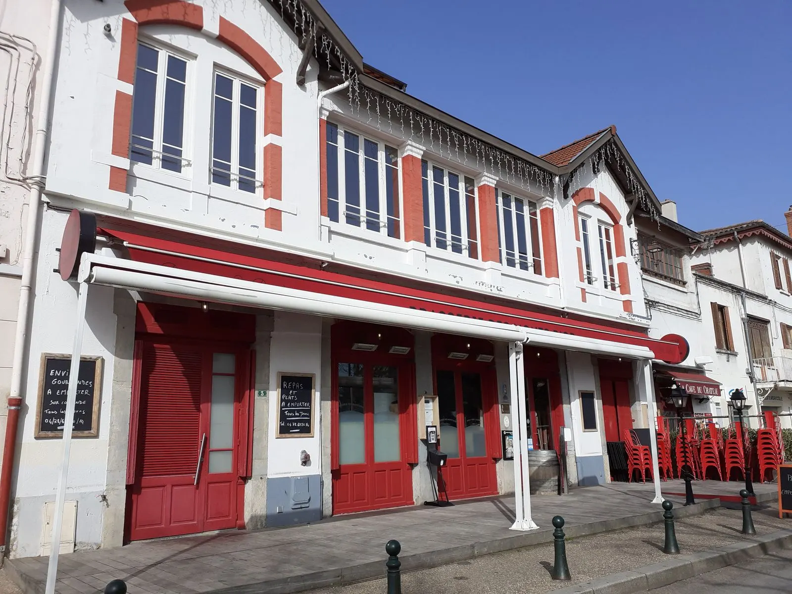 La façade de La Brasserie des Monts d'Or de jour, store et devanture rouges sur la place du village
