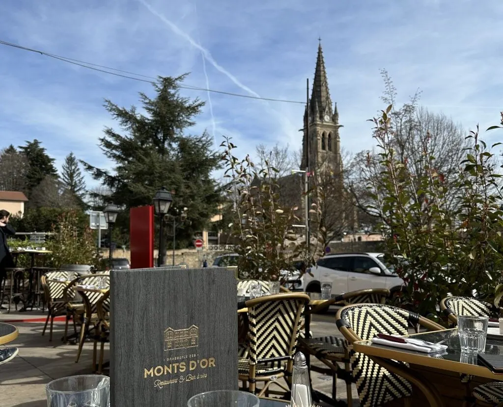 La terrasse de la brasserie face au clocher de Saint-Cyr-au-Mont-d'Or sous un ciel bleu
